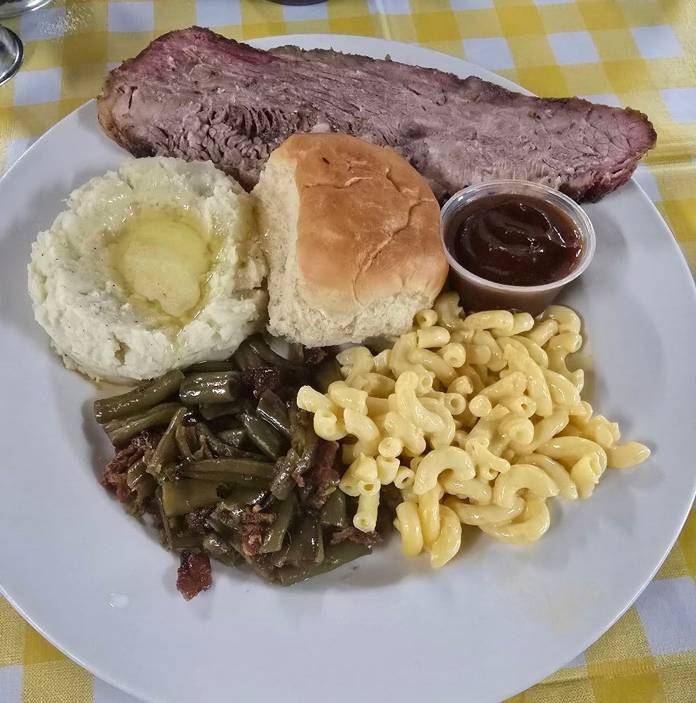 Plate of barbecue brisket with mashed potatoes, roll, baked beans, green beans, and macaroni and cheese