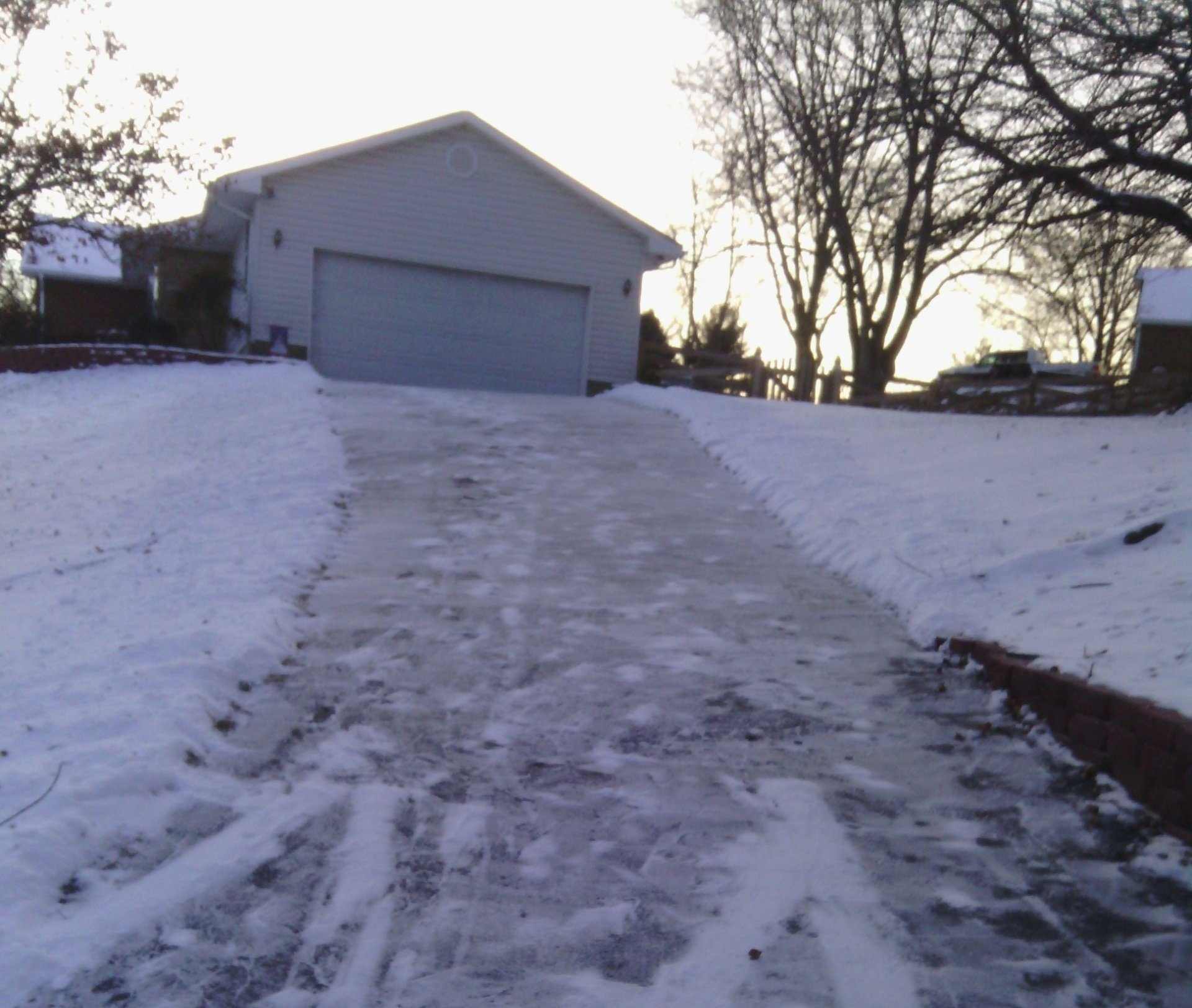 A snowy driveway with a garage in the background