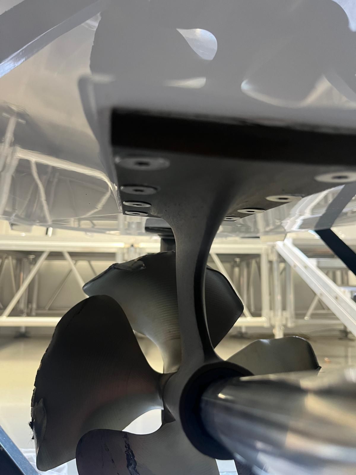 A close-up view of a boat's metal propeller and its mounting strut attached to the underside of the white hull. — Ocean Mate Marine Services in Brisbane, QLD