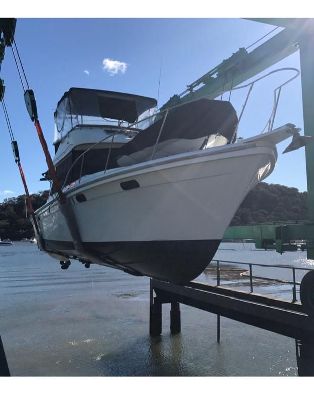A white boat is hoisted into the air by a metal crane structure above a body of water on a sunny day — Ocean Mate Marine Services in Coomera, QLD
