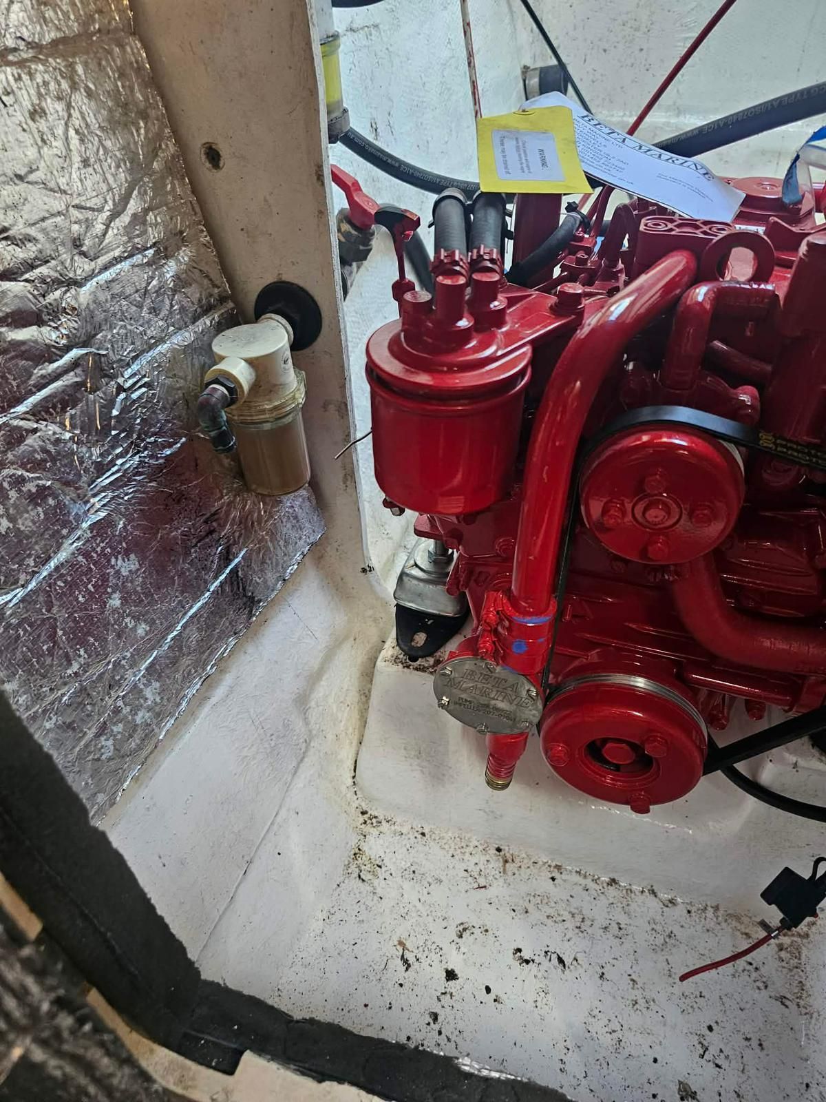 A marine engine with red components sits in a white compartment next to a white plastic fuel filter on a silver wall. — Ocean Mate Marine Services in Coomera, QLD
