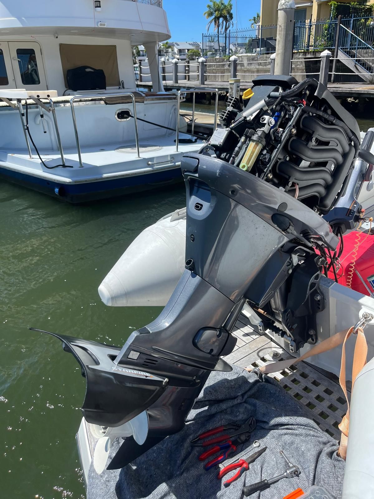 A gray outboard boat motor with its housing removed, sitting on a boat deck with tools nearby near a docked yacht. — Ocean Mate Marine Services in Coomera, QLD