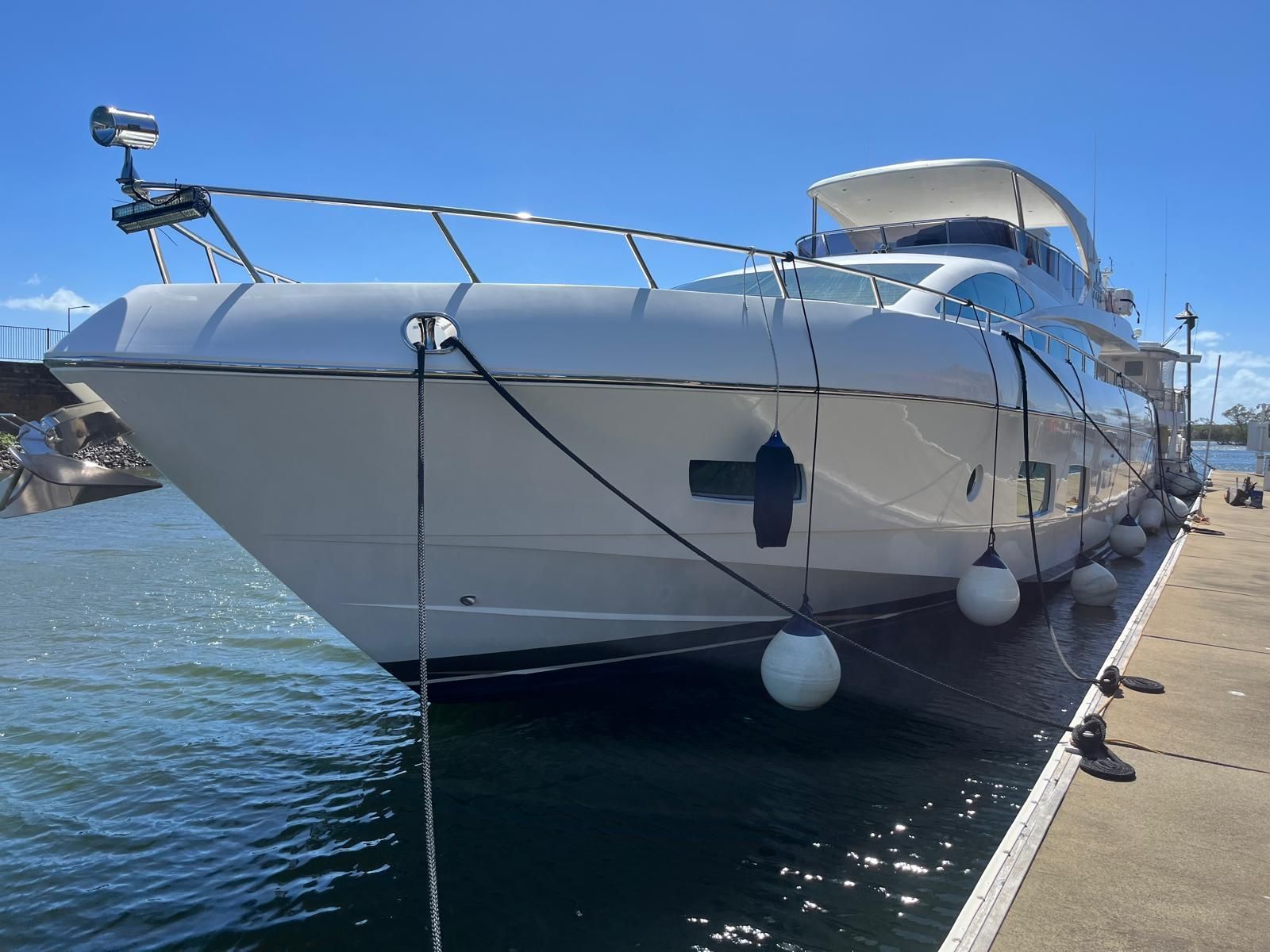 A white motor yacht docked at a concrete pier on a clear, sunny day — Ocean Mate Marine Services in Coomera, QLD