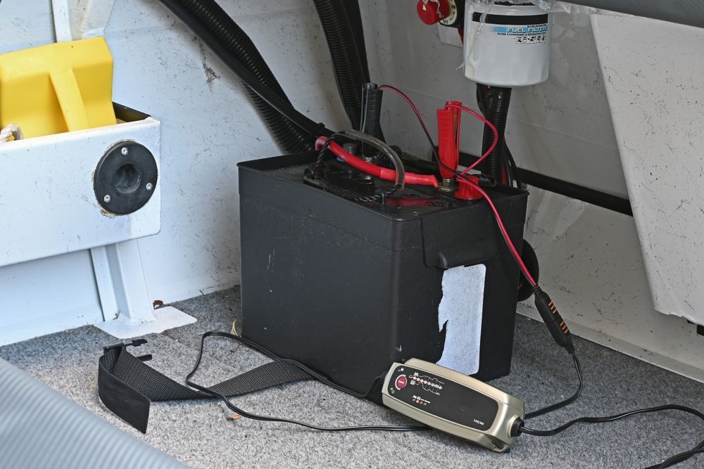 A battery charging setup in a boat storage compartment with a black battery and a connected charger — Ocean Mate Marine Services in Coomera, QLD