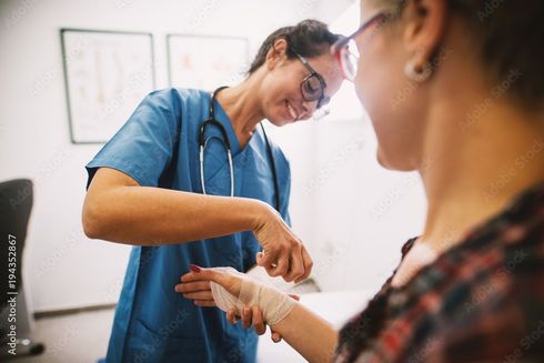 A nurse is bandaging a patient 's hand in a hospital.