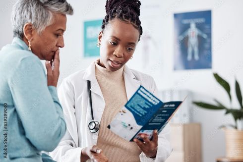 A doctor is talking to an older woman while holding a brochure.
