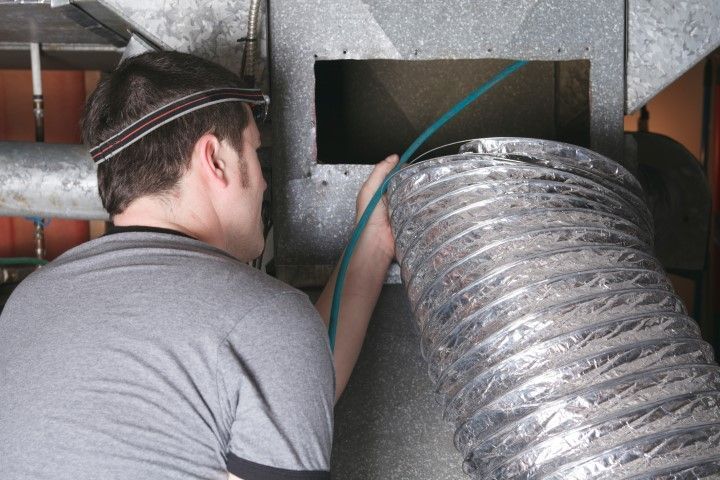 A man is working on an air duct with a hose.