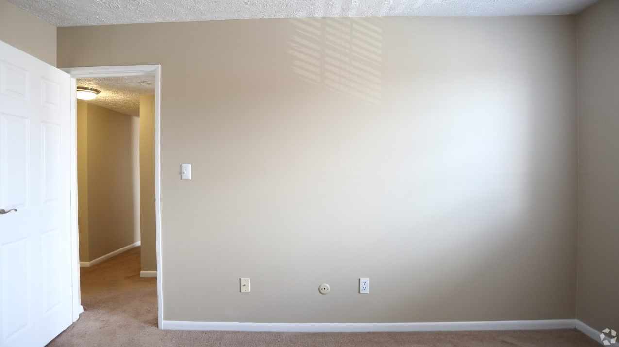 An empty bedroom with a door open and a carpeted floor.