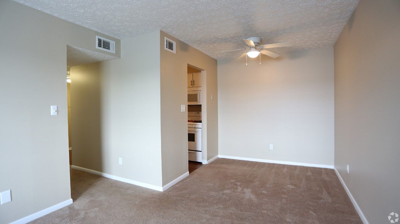 An empty living room with a ceiling fan and a doorway leading to a kitchen.
