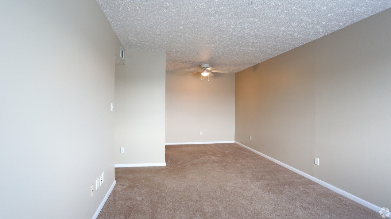 An empty living room with a ceiling fan and a brown carpet.
