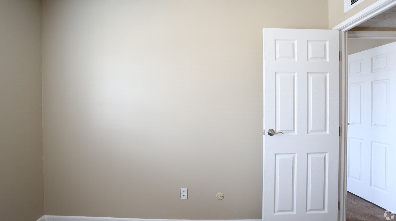 An empty room with a white door and beige walls.