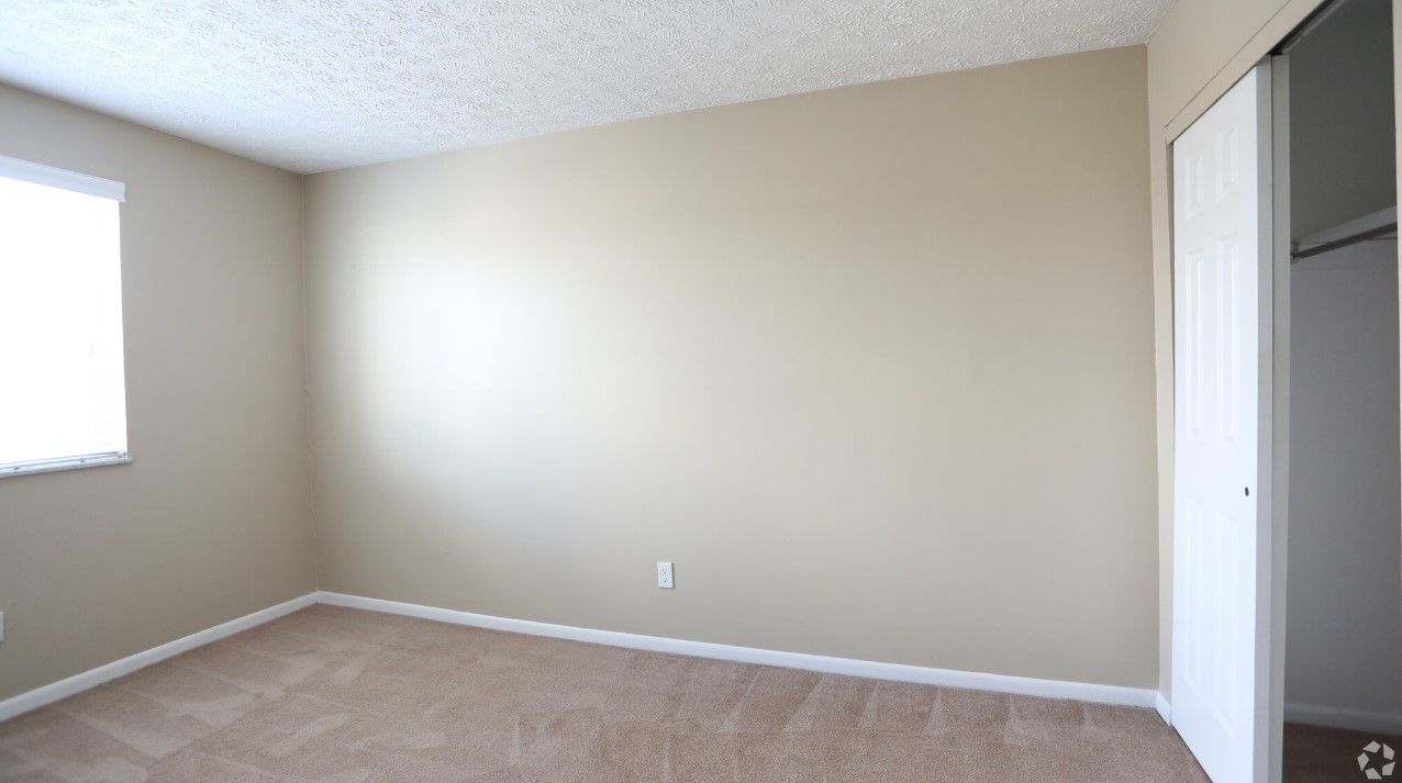 An empty bedroom with a window and a closet.