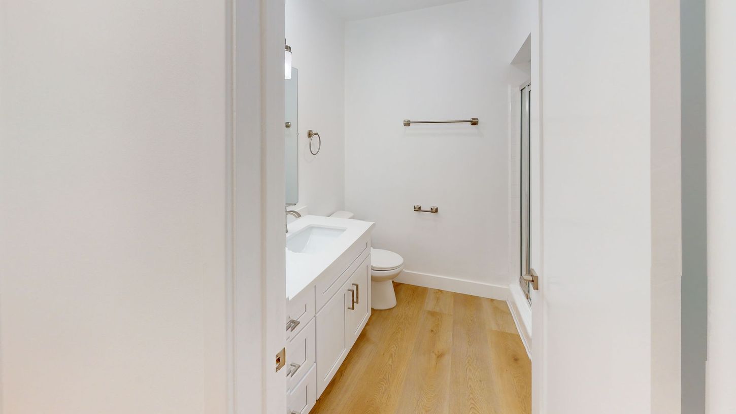 White bathroom with vanity, toilet, and shower, light wood floor.