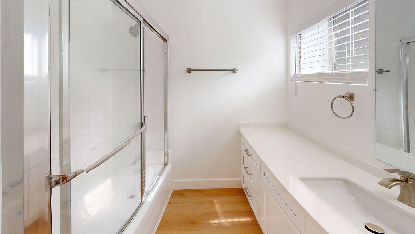Bright white bathroom with a shower, countertop, cabinets, and a window.