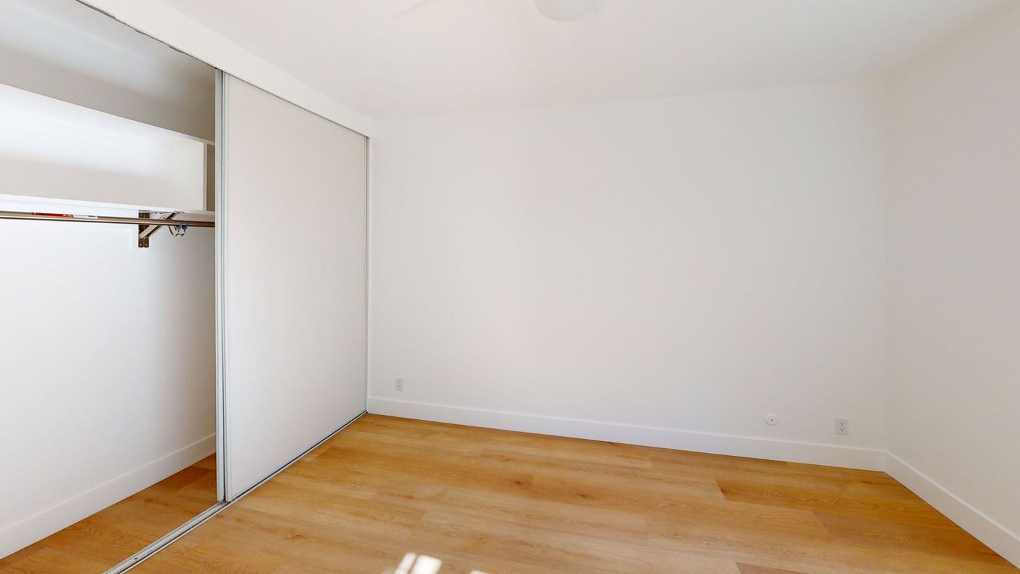 Empty room with white walls, sliding closet doors, and hardwood floors.