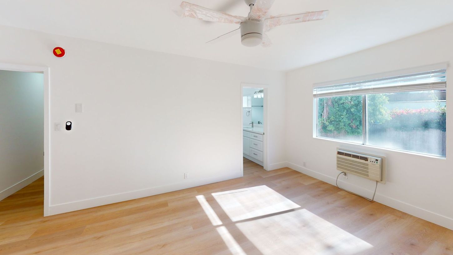 Bright room with wood floor, white walls, ceiling fan, and window with air conditioner.