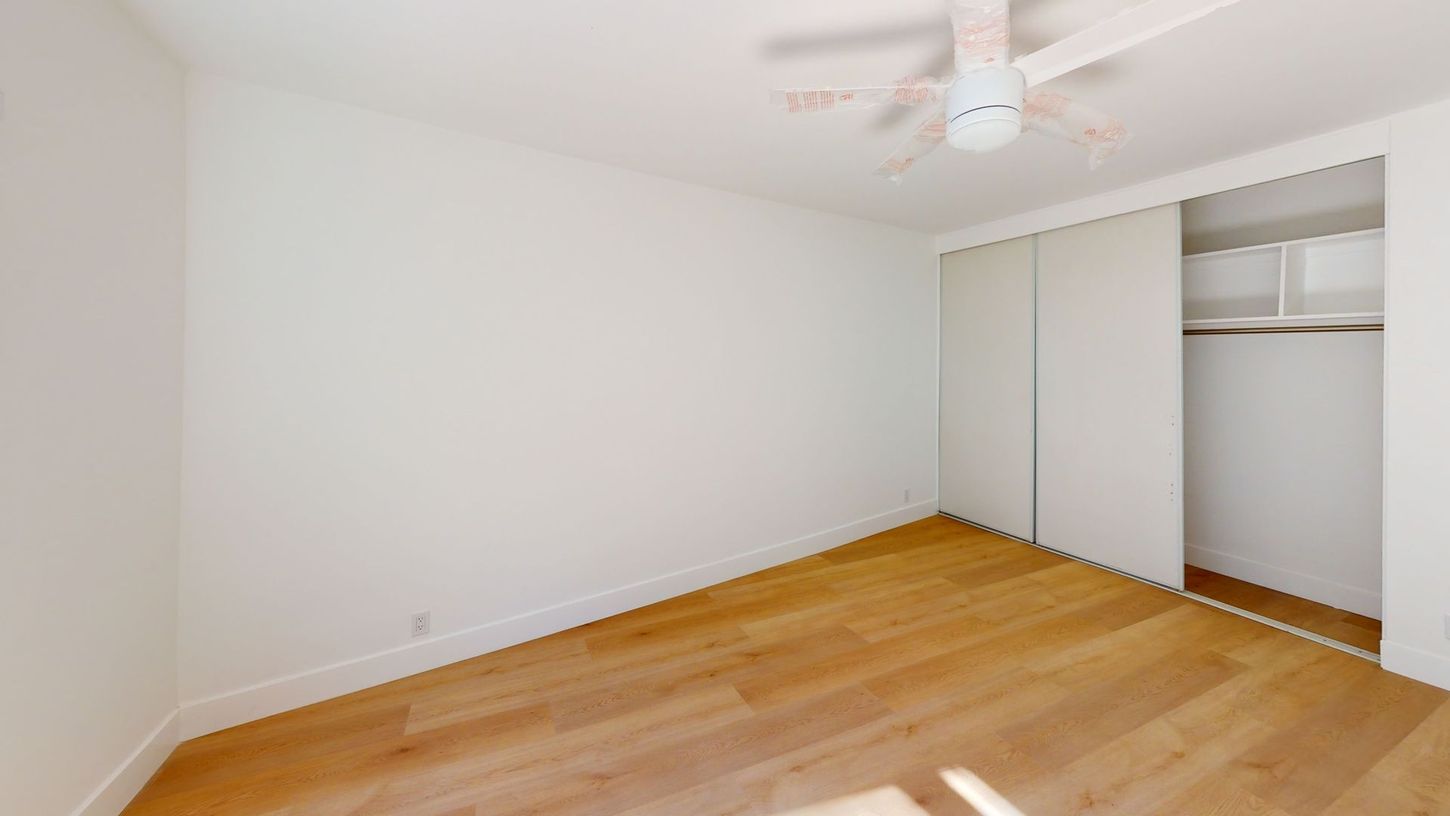 Empty room with hardwood floors, white walls, closet, and ceiling fan.