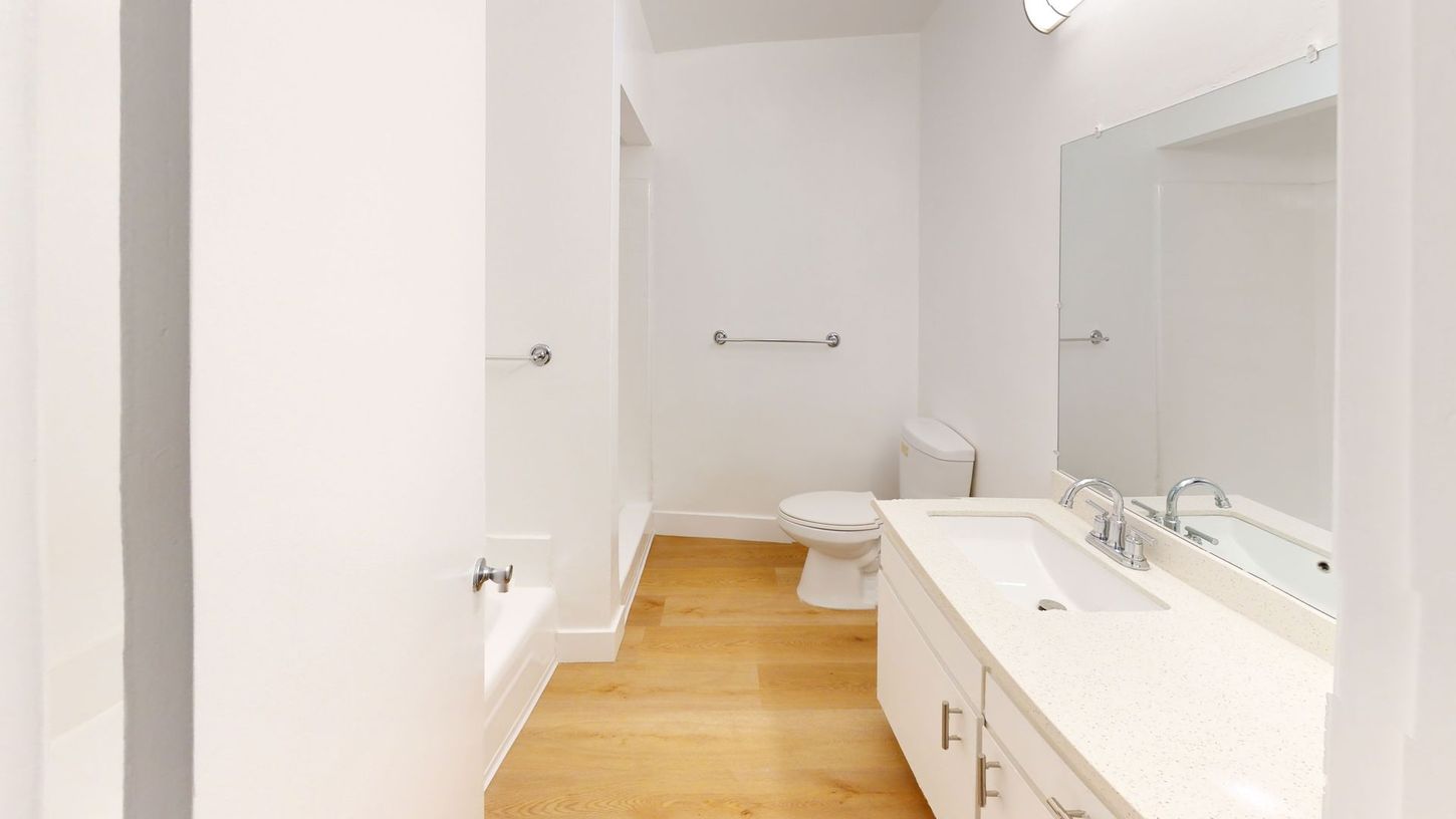 White bathroom with wood floor, toilet, vanity, and large mirror.