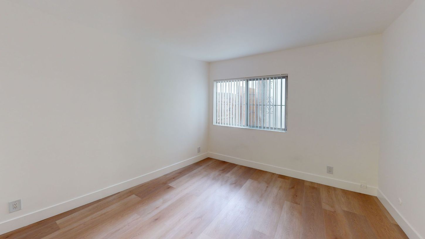 Empty room with hardwood floors, a window with blinds, and white walls.