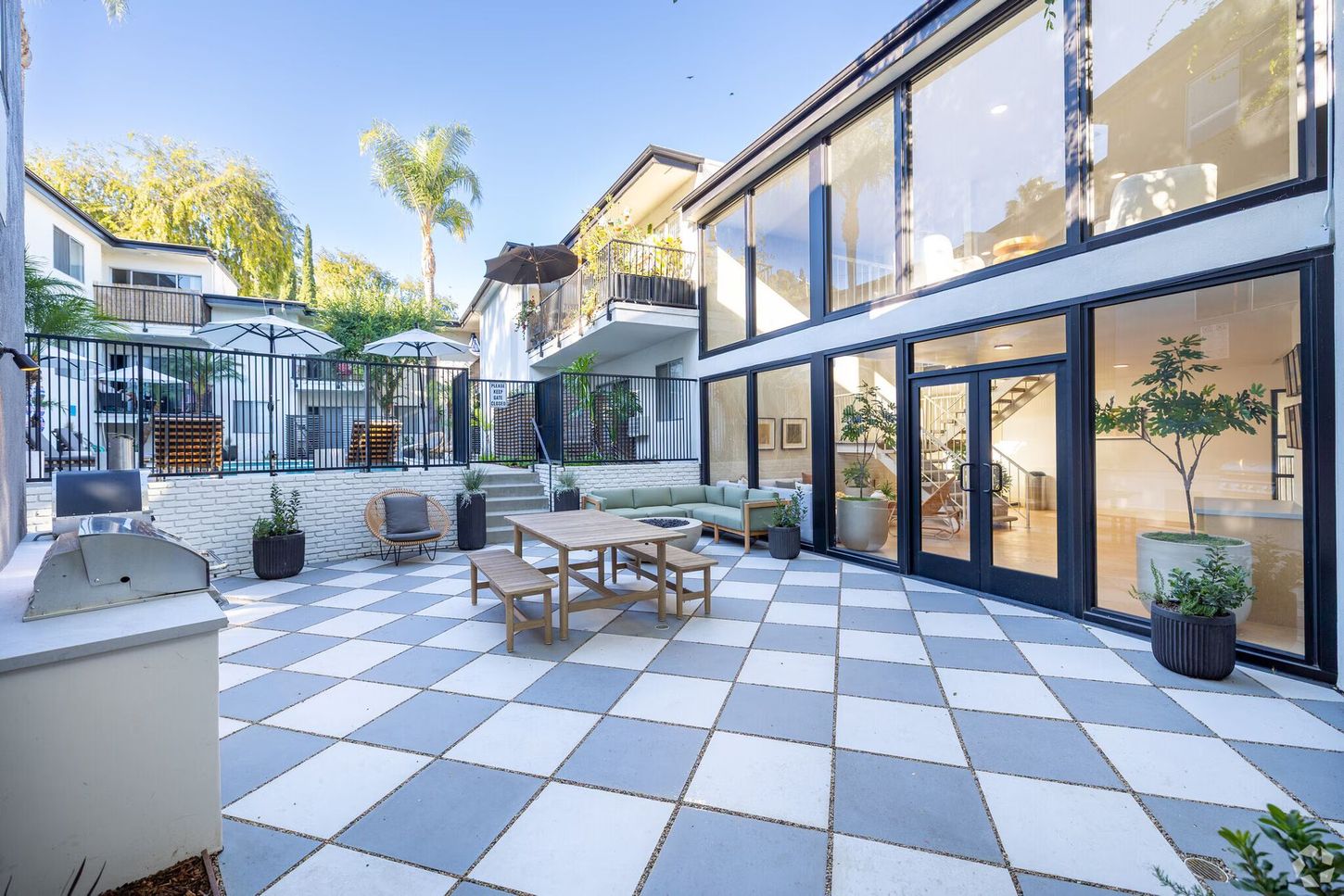 Patio with checkered floor, outdoor dining set, large windows, and pool area.