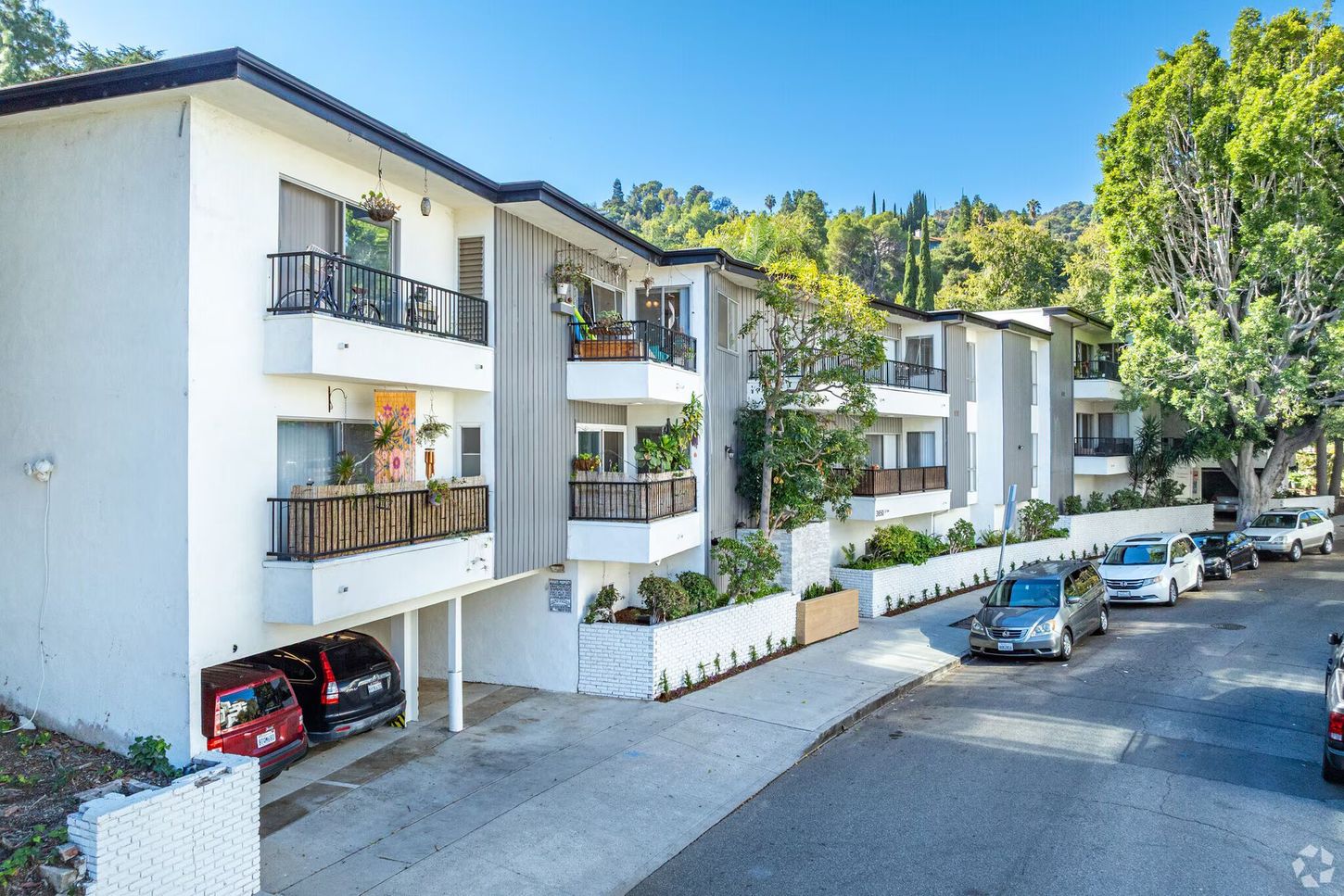 Apartment building with white facade and balconies on a street with parked cars.