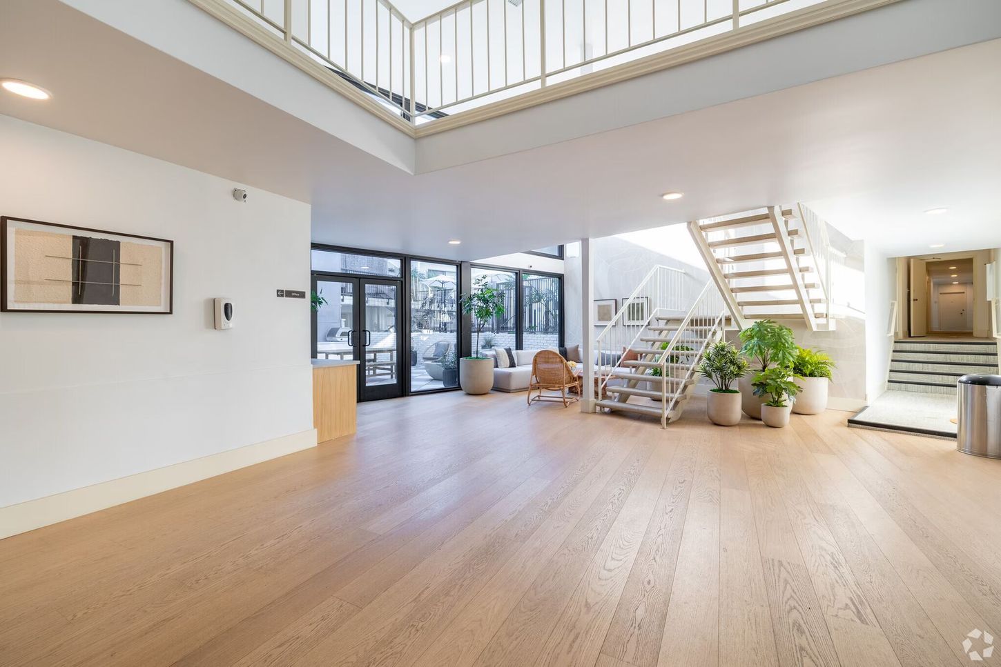 Bright entry hall with wooden floors, staircase, and glass doors leading outside.