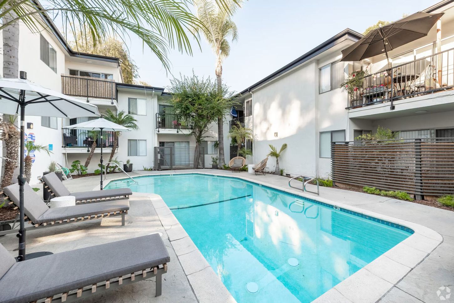 Pool area with chaise lounges, umbrellas, and apartment buildings.