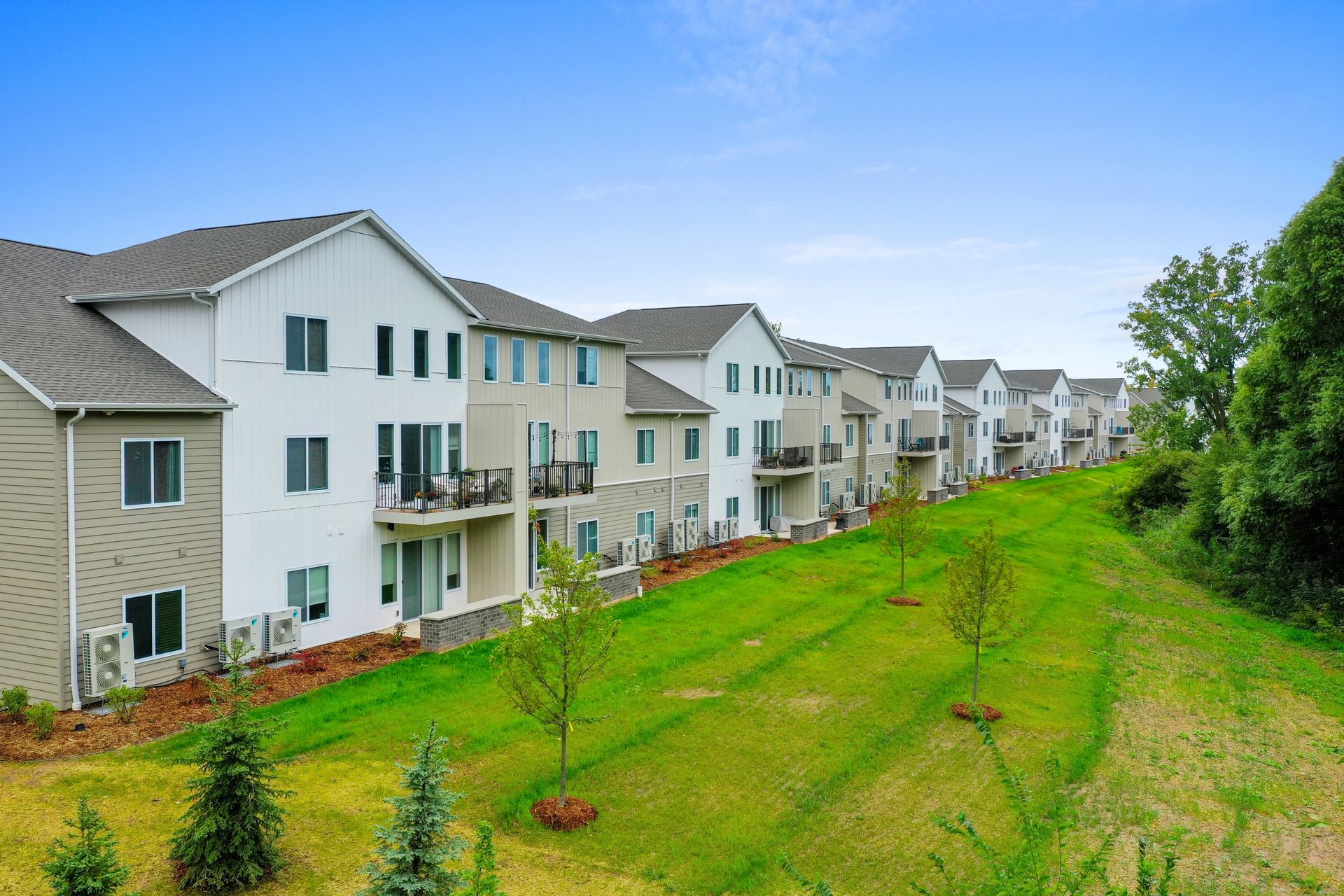 Row of white apartment buildings beside a green grassy slope under a blue sky