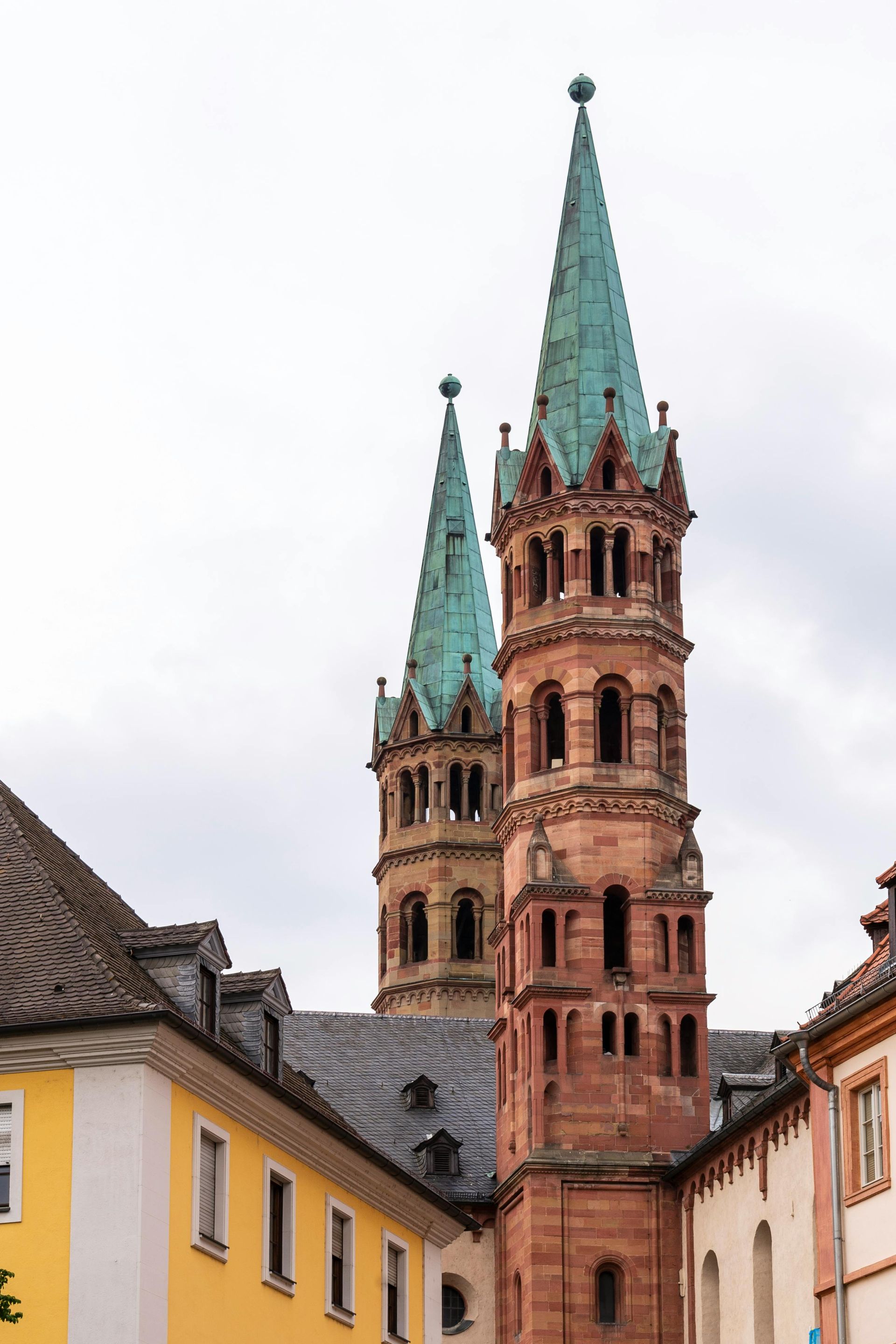 Two tall, tiered towers with turquoise spires rise above the roofs of yellow and white historic stone buildings.