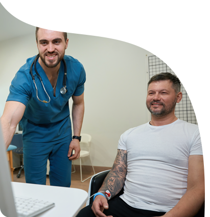 A doctor is standing next to a man sitting in front of a laptop computer.