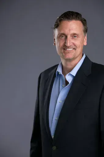 A man in a suit and blue shirt is smiling for the camera.