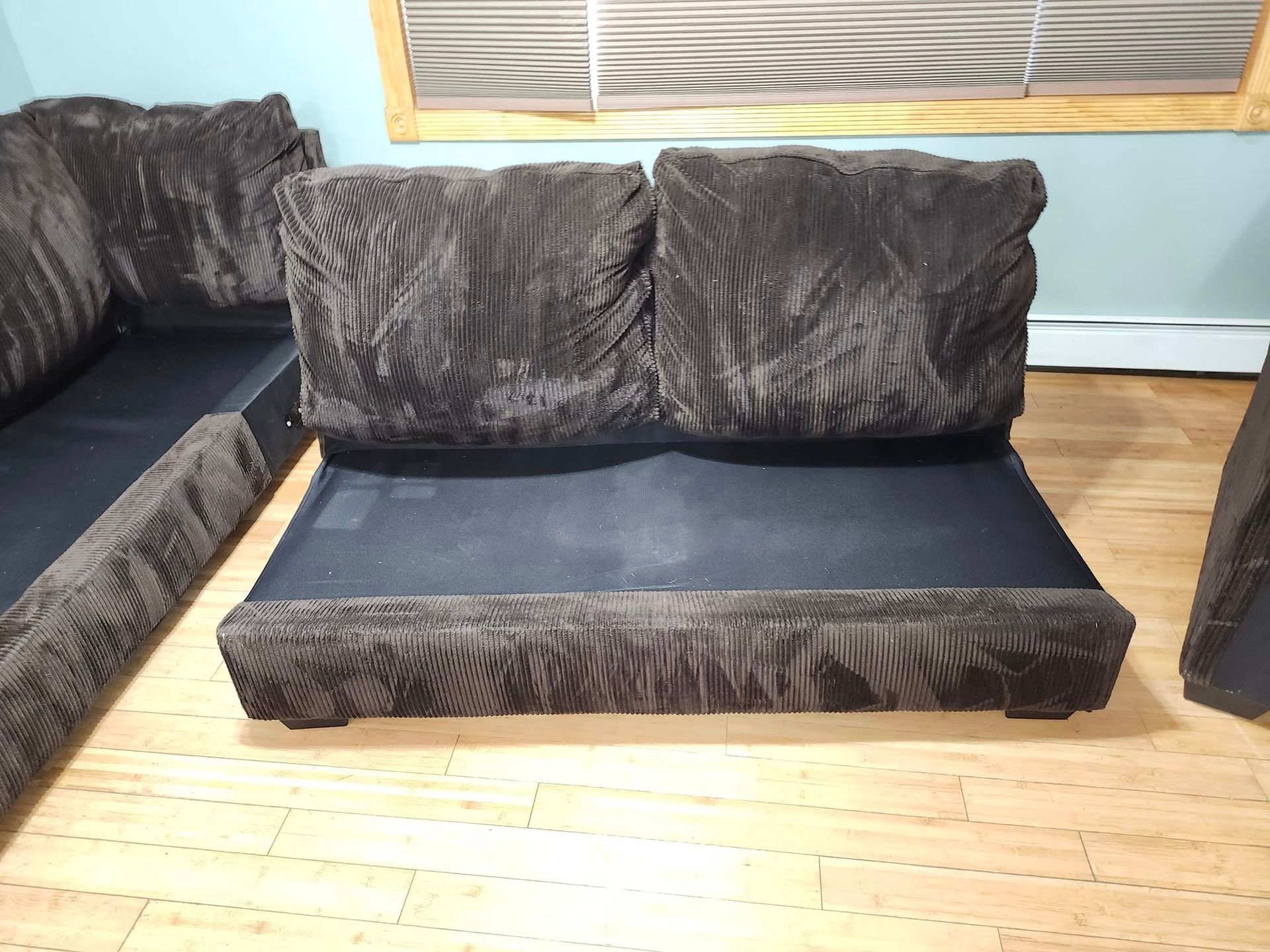 Brown sectional sofa with fluffy cushions on a wooden floor.