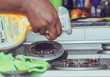 Hand spraying cleaner on a greasy stovetop near a kitchen sink