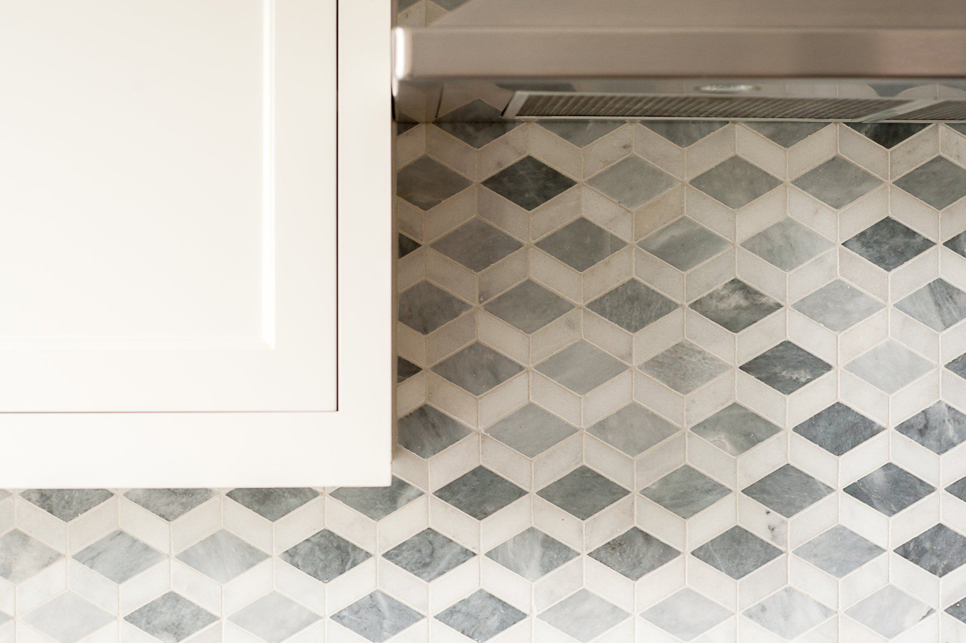 A kitchen with a gray and white tile wall and a white cabinet.