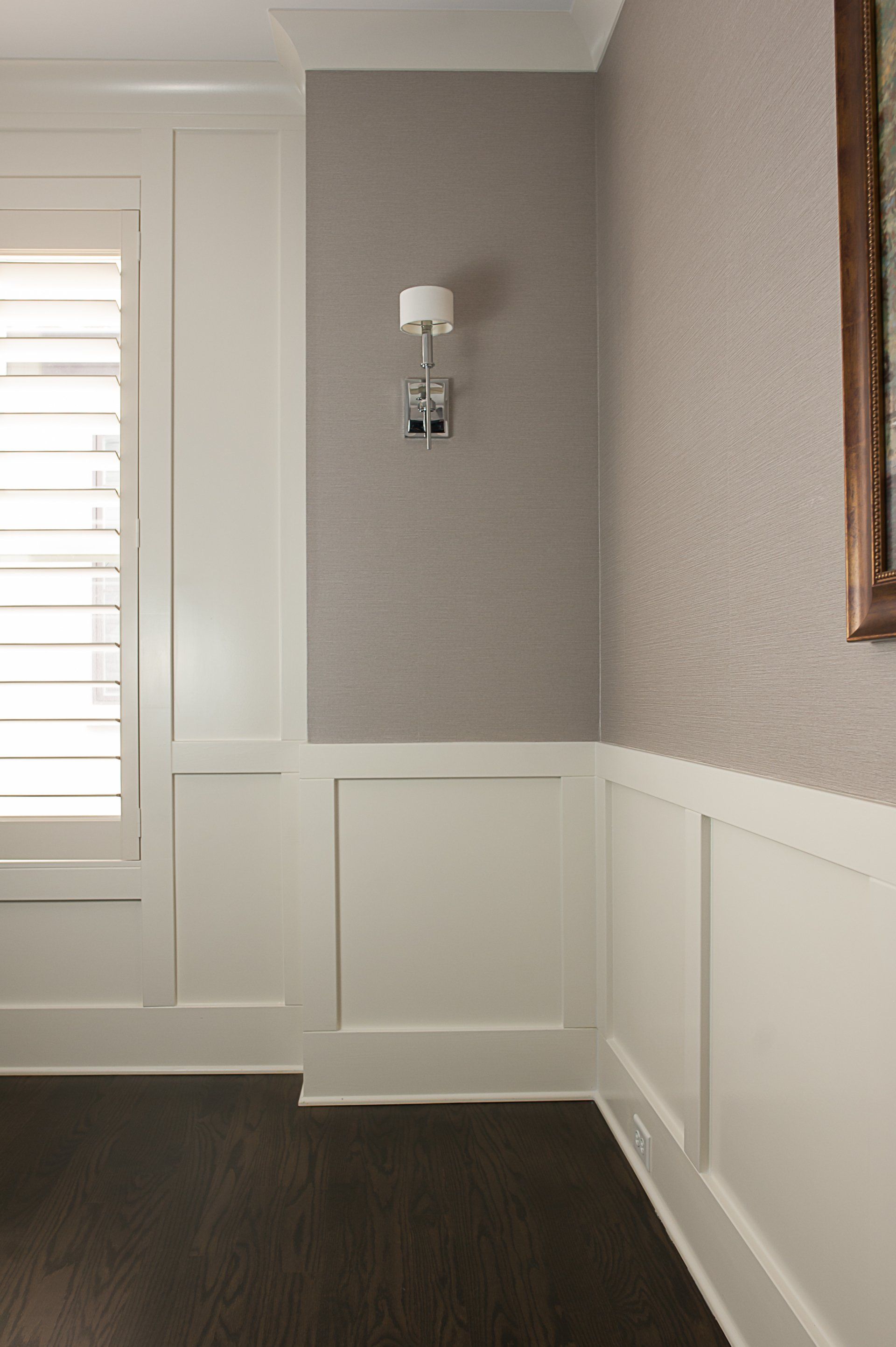 A hallway with white paneling , a window , and a picture on the wall.
