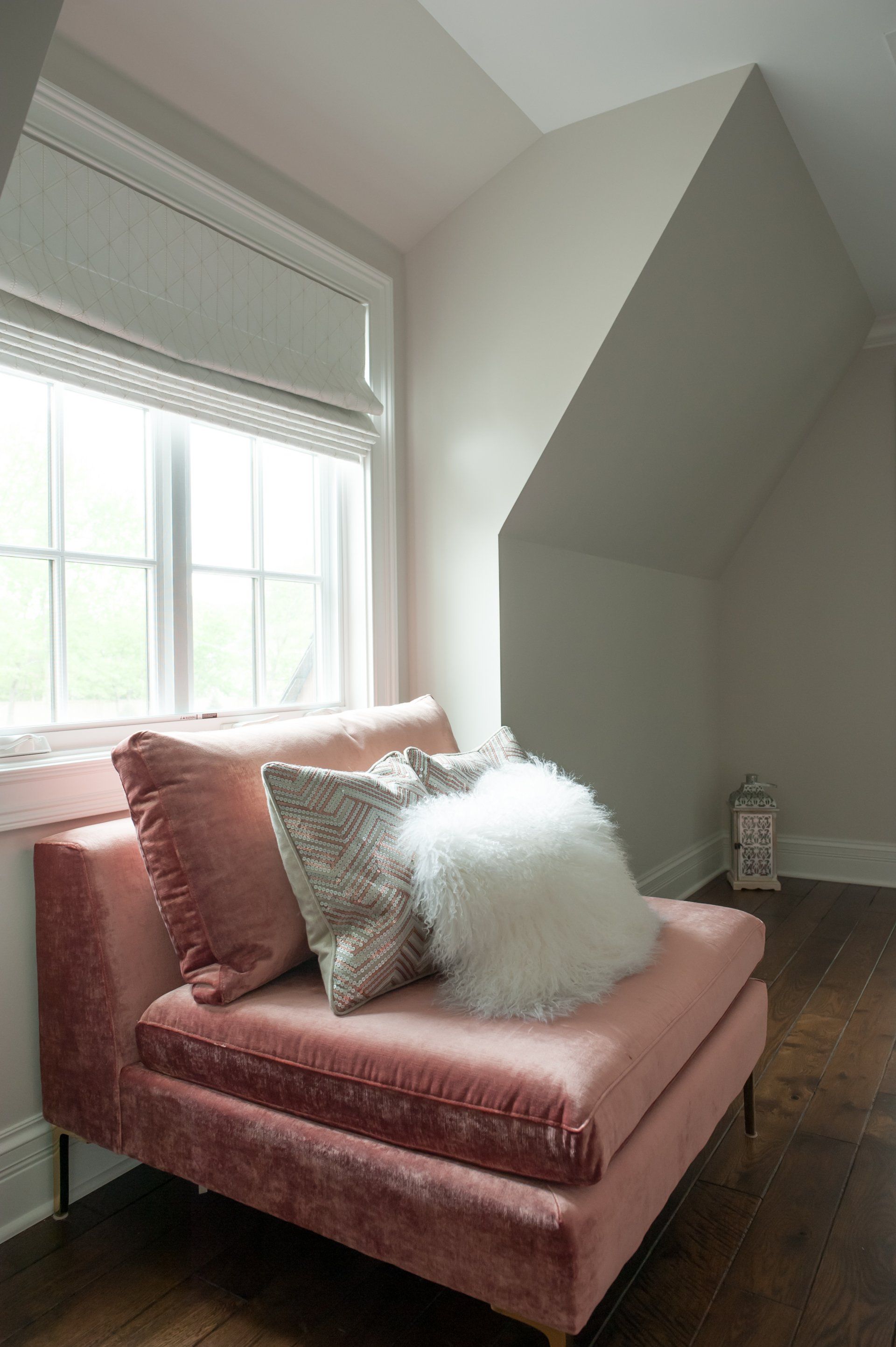 A pink couch with white pillows is sitting in front of a window in a room.