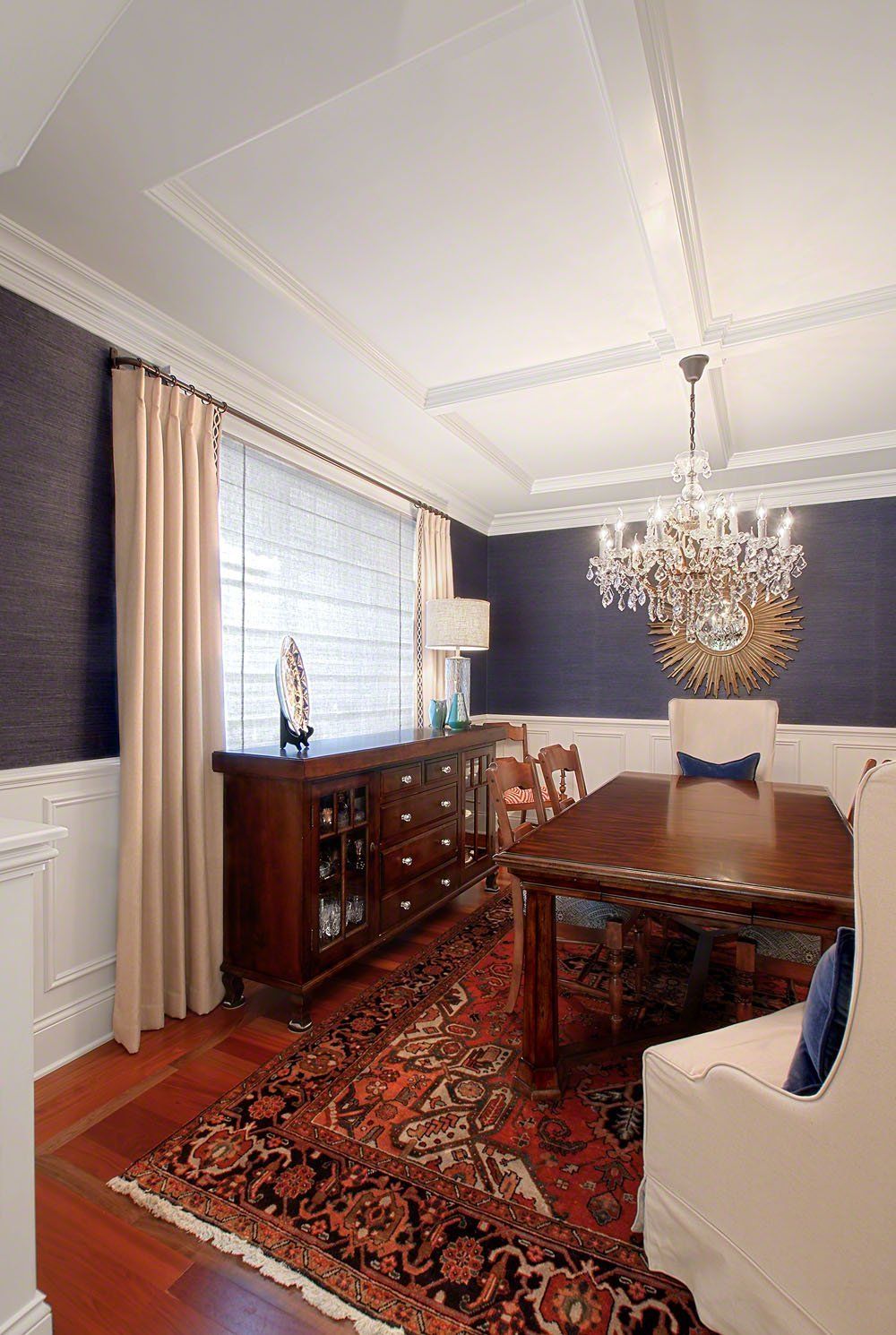 A dining room with a table , chairs , a rug and a chandelier.
