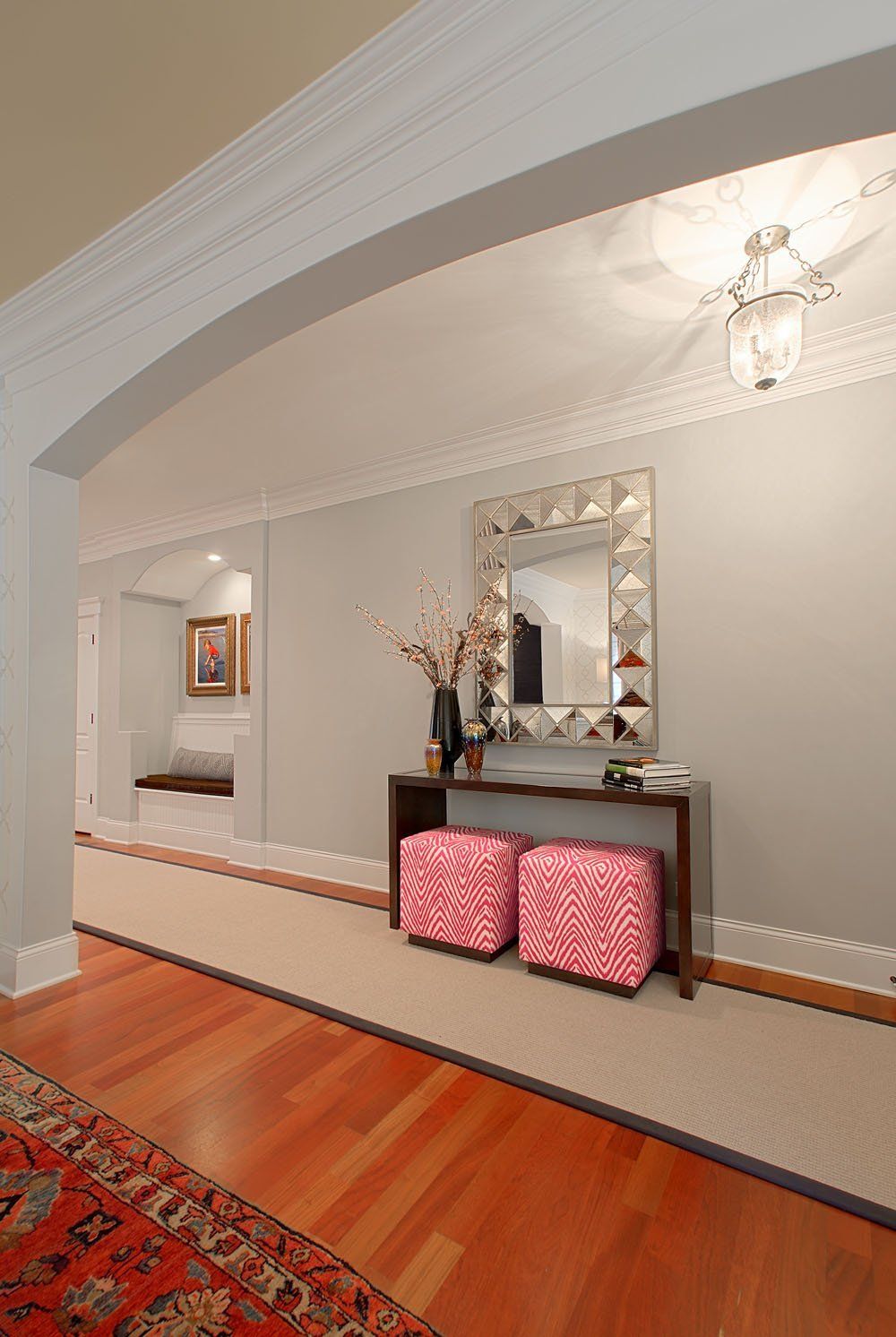 A hallway with two pink ottomans and a mirror