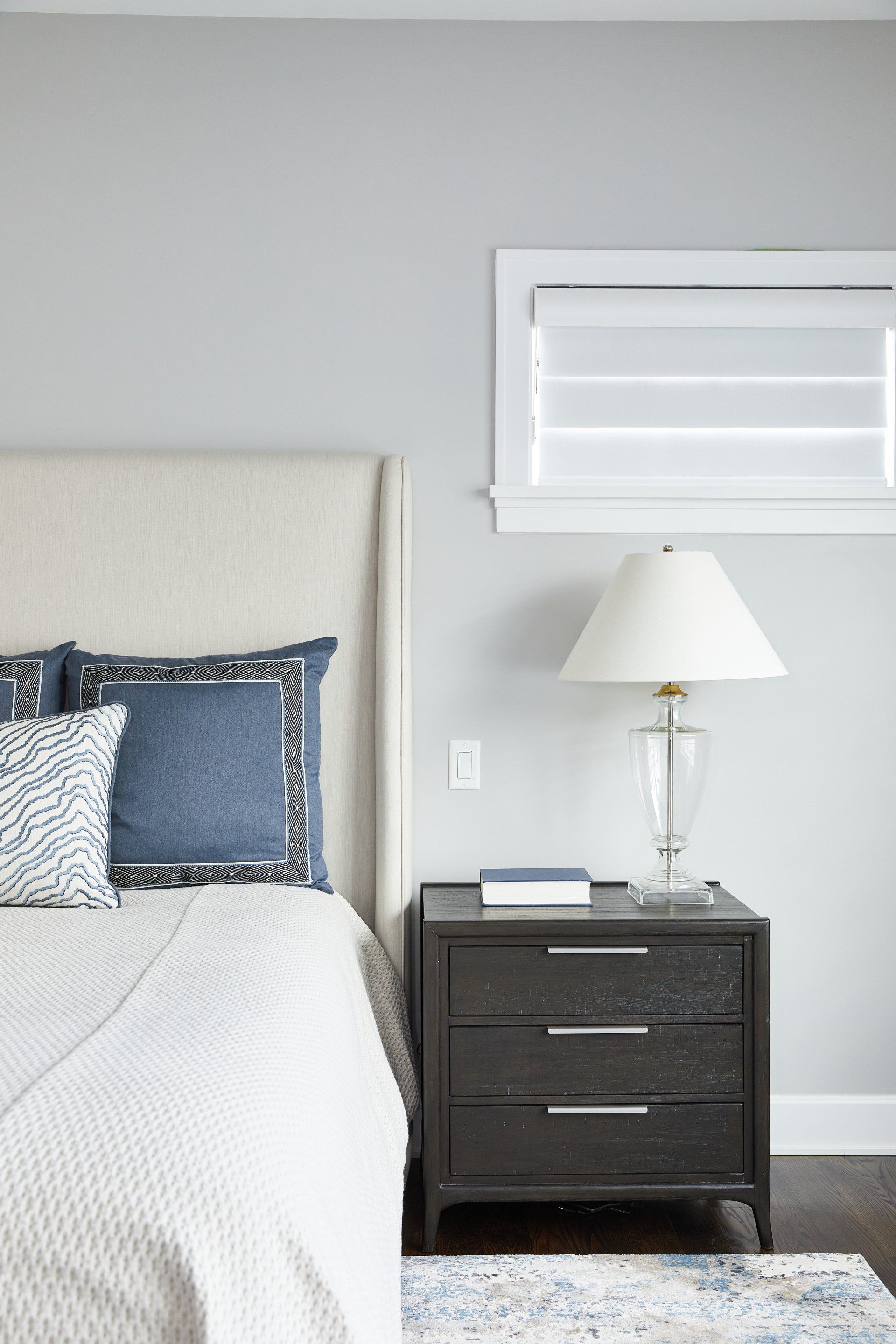 A bedroom with a bed , nightstand , lamp and window.