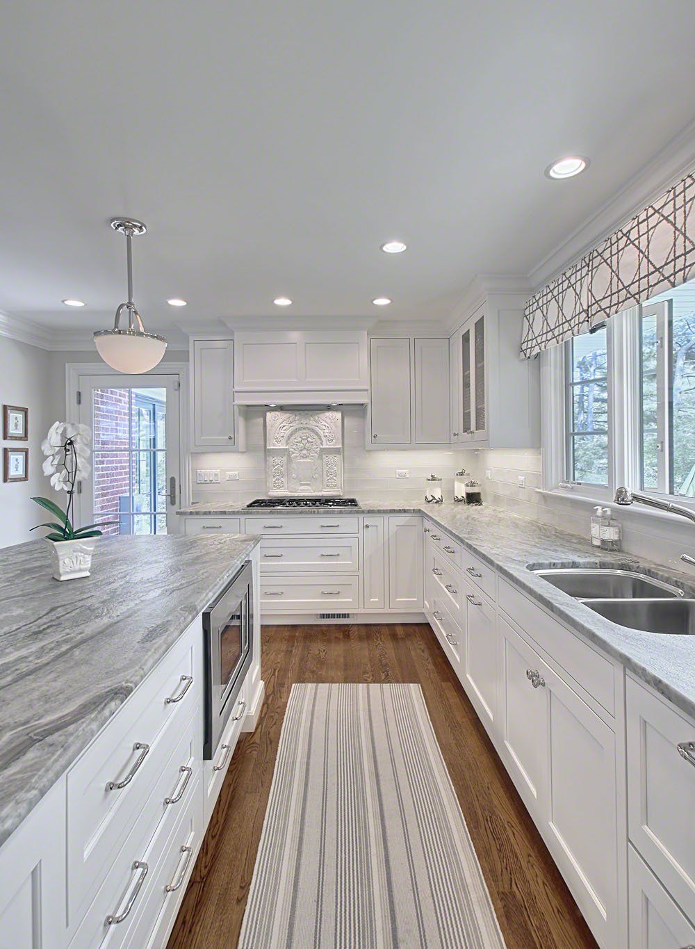 A kitchen with white cabinets , granite counter tops , and a rug on the floor.