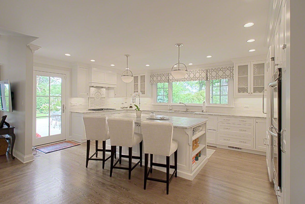 A kitchen with white cabinets and stools and a large island.