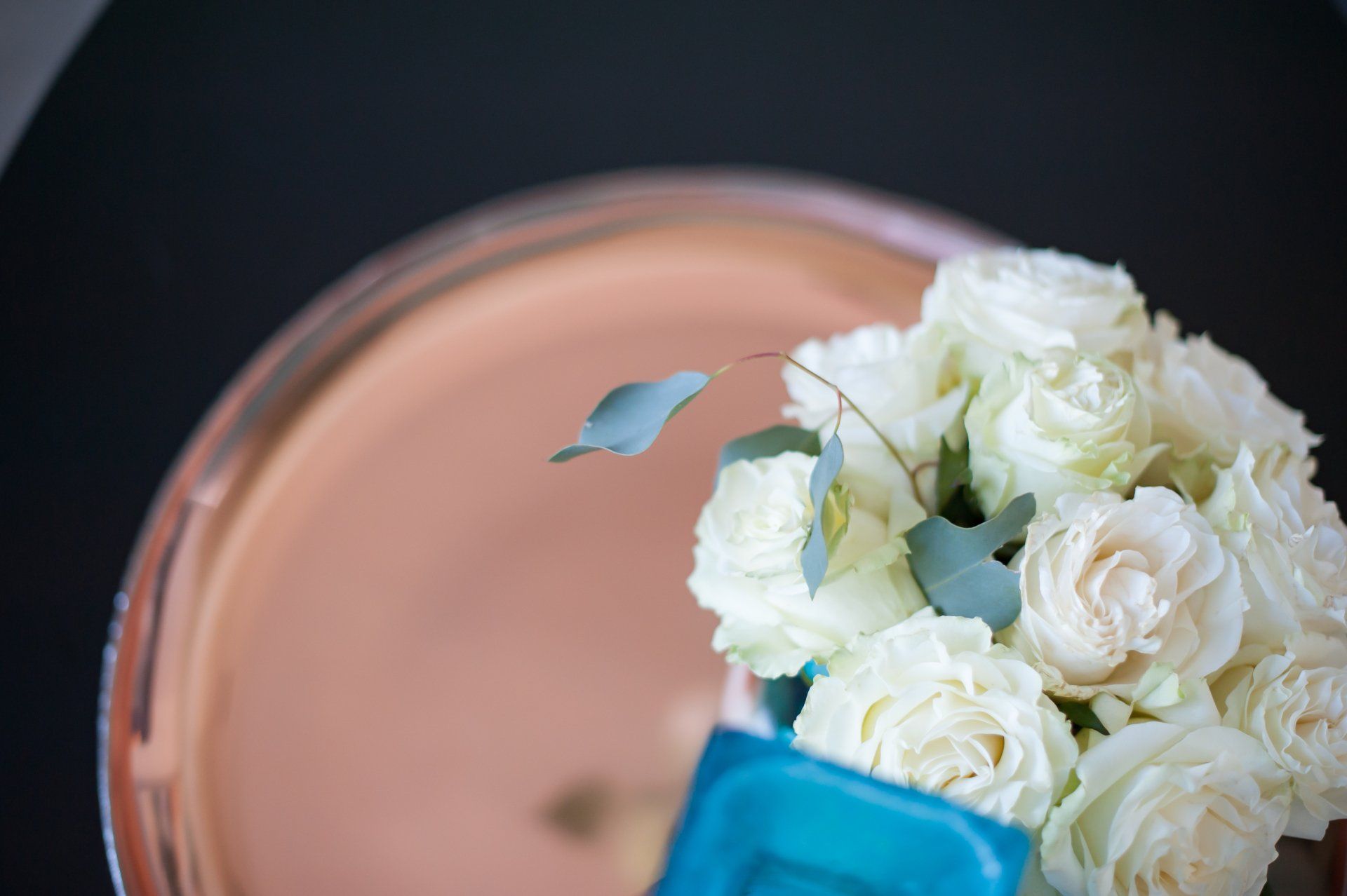 A bouquet of white roses in a blue vase on a copper plate.