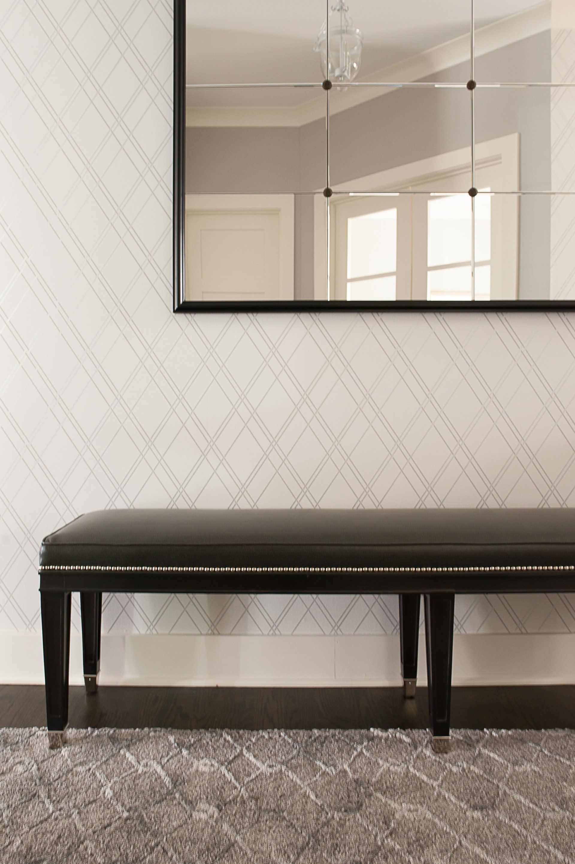 A black bench is sitting under a large mirror in a hallway.