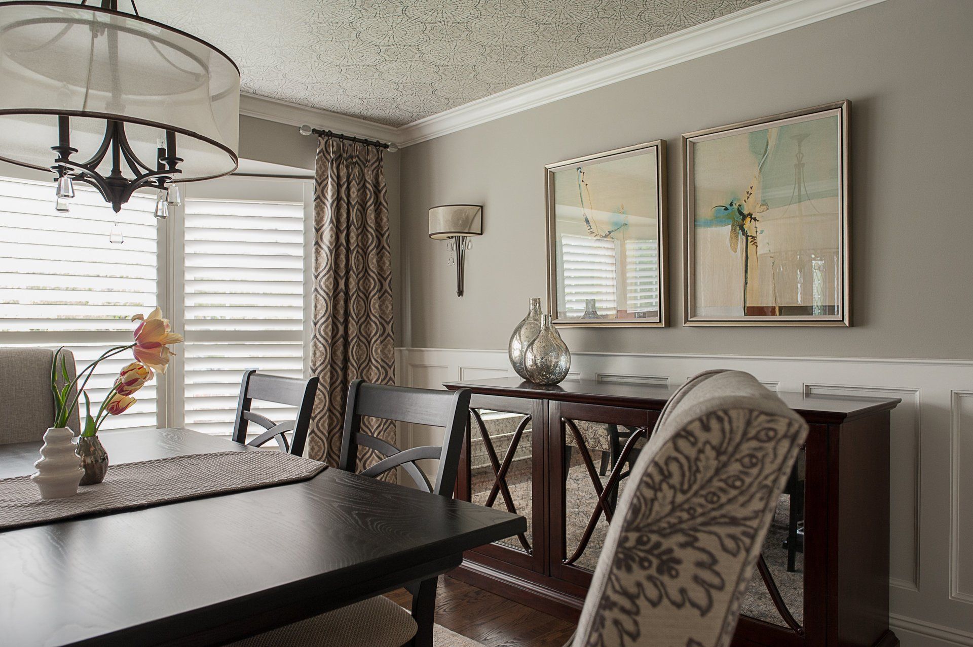 A dining room with a table and chairs and two mirrors on the wall.