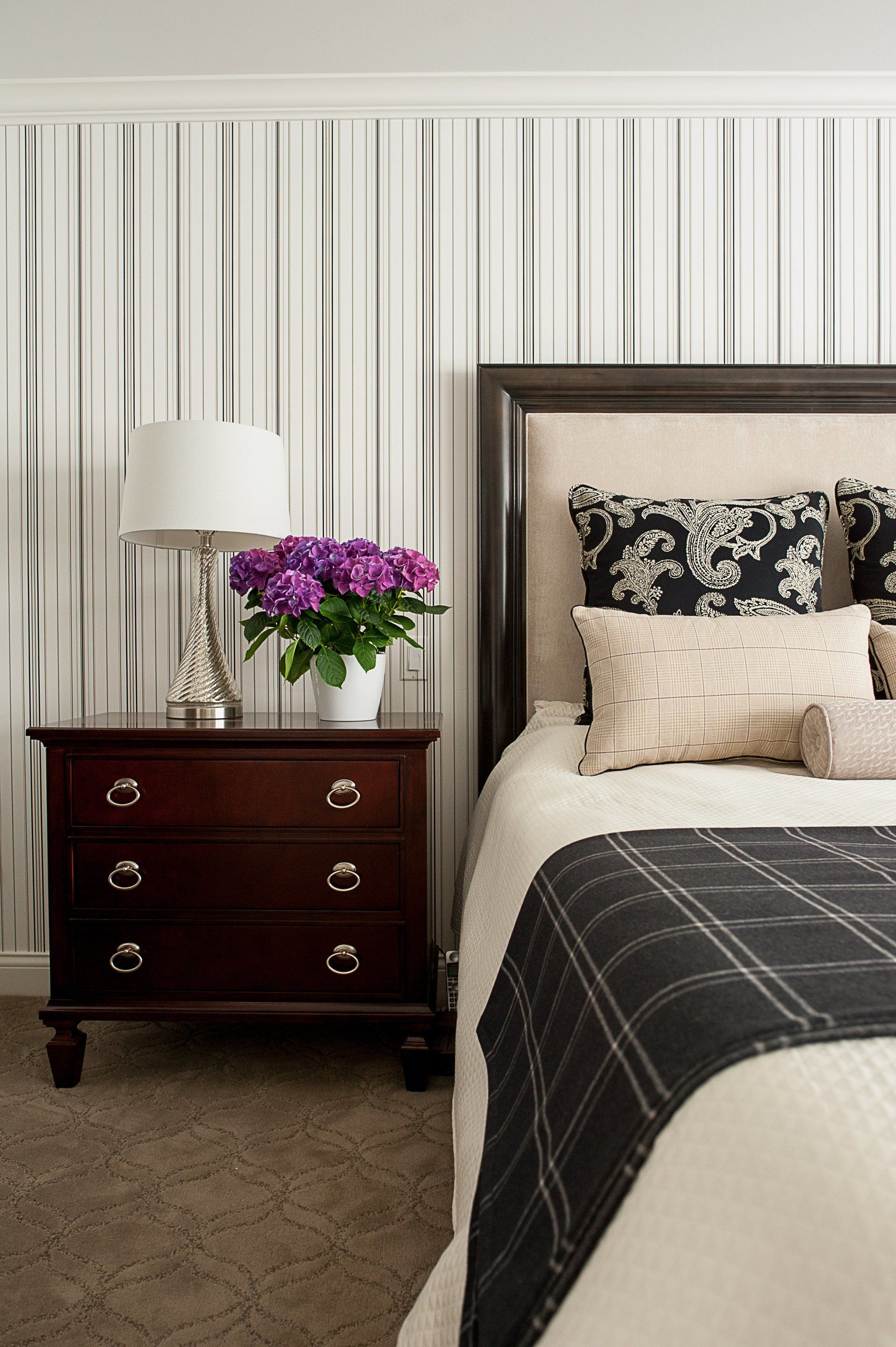 A bedroom with a bed , nightstand , lamp and striped wallpaper.