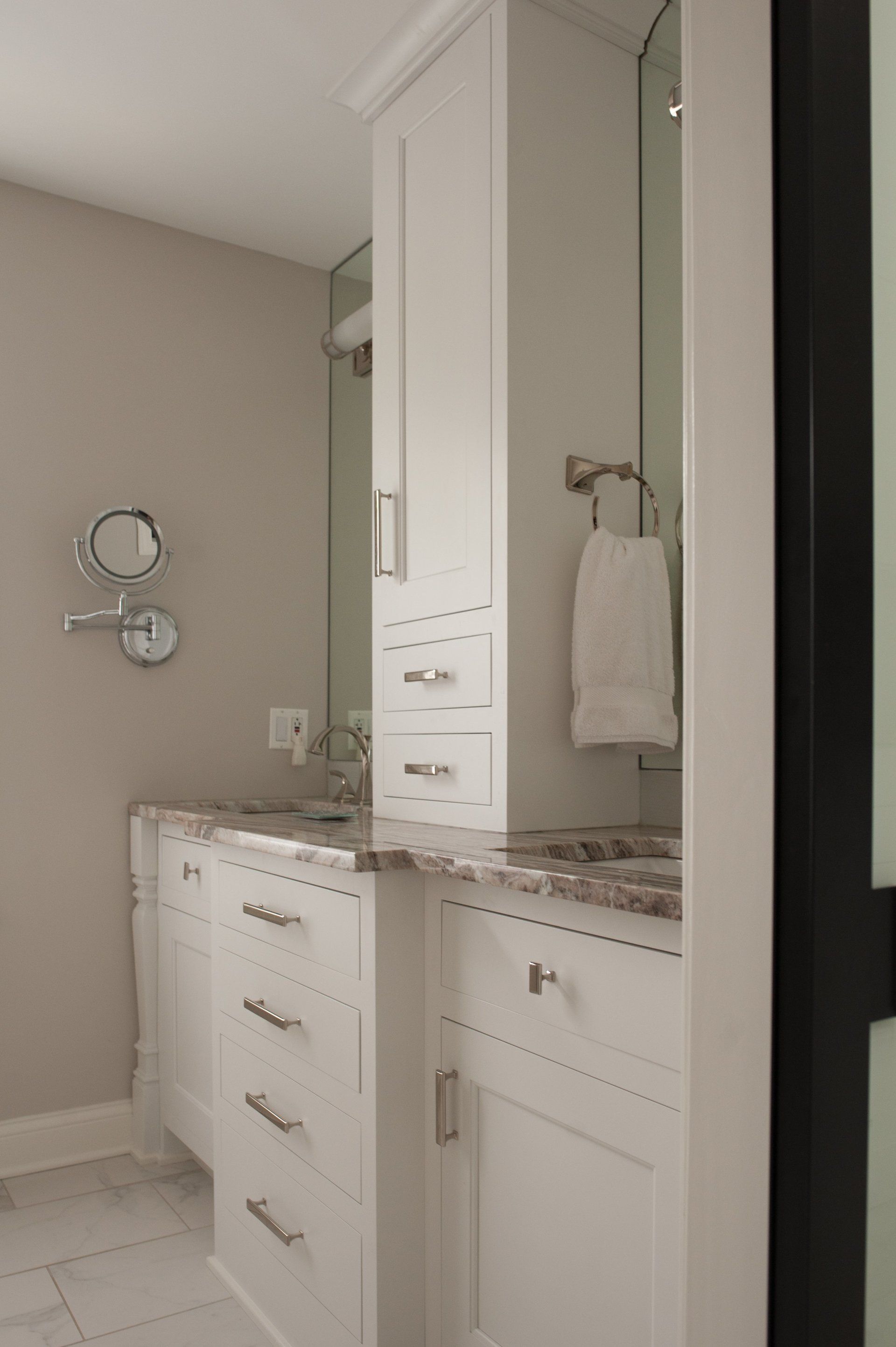 A bathroom with white cabinets , a sink , a mirror and a towel rack.
