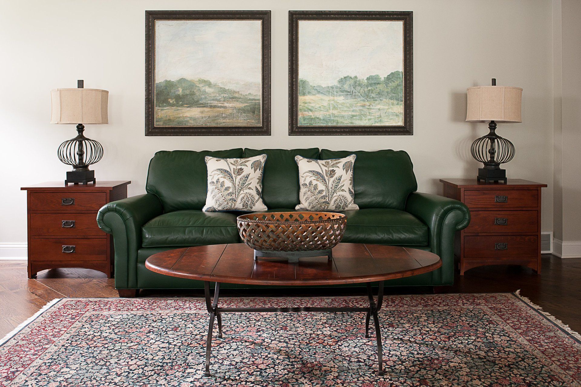 A living room with a green couch , two lamps , a coffee table and two paintings on the wall.