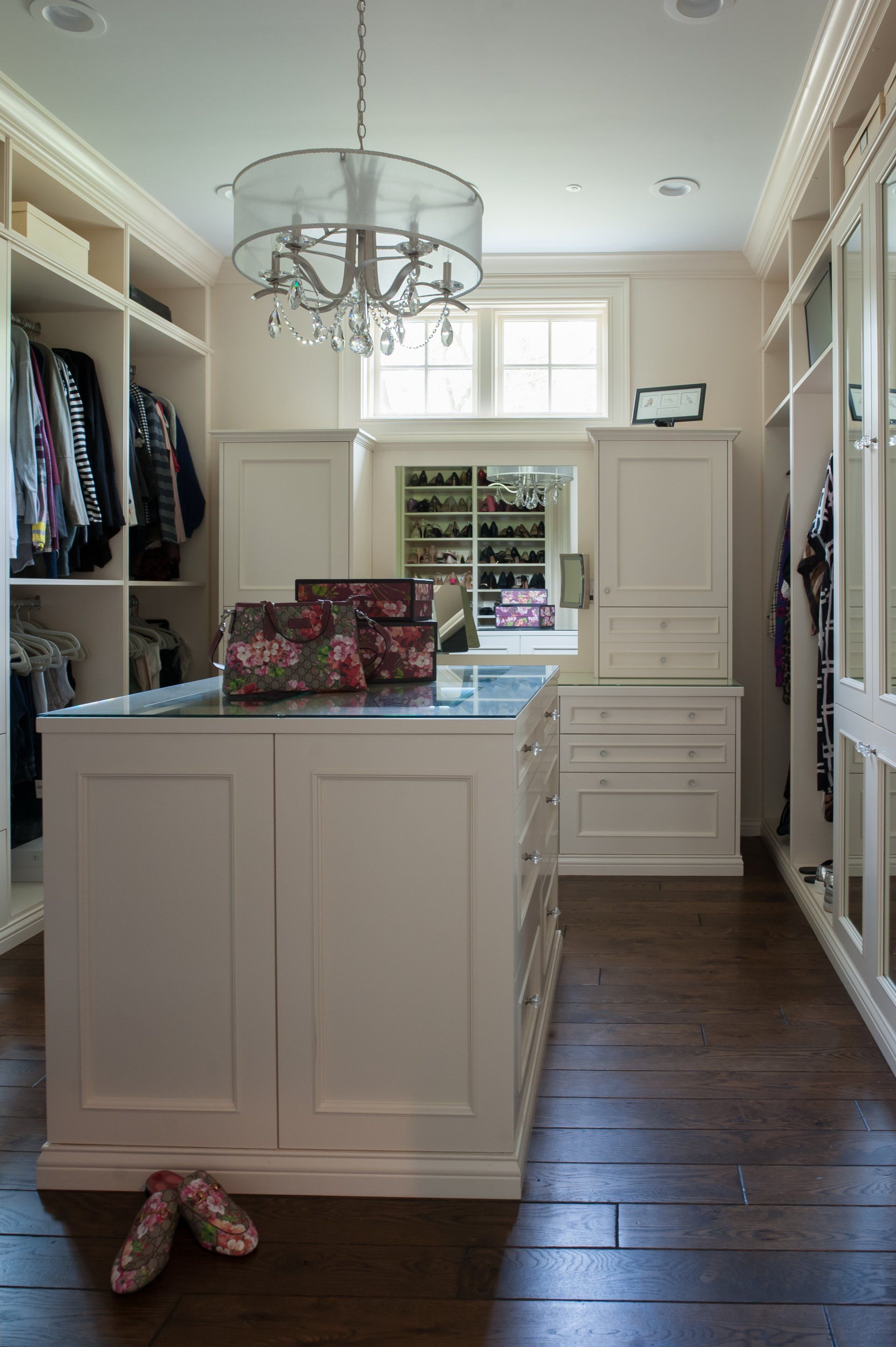 A walk in closet with a large island in the middle and a chandelier hanging from the ceiling.