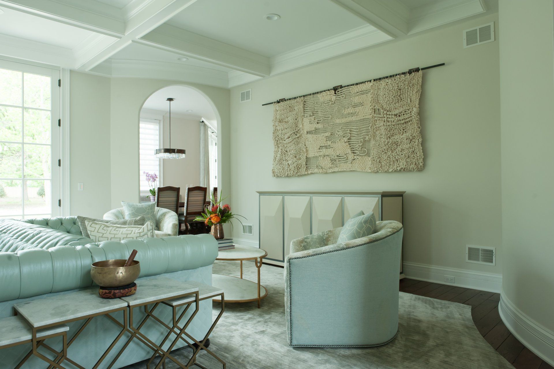 A living room with a blue couch , two chairs , a coffee table and a large tapestry on the wall.
