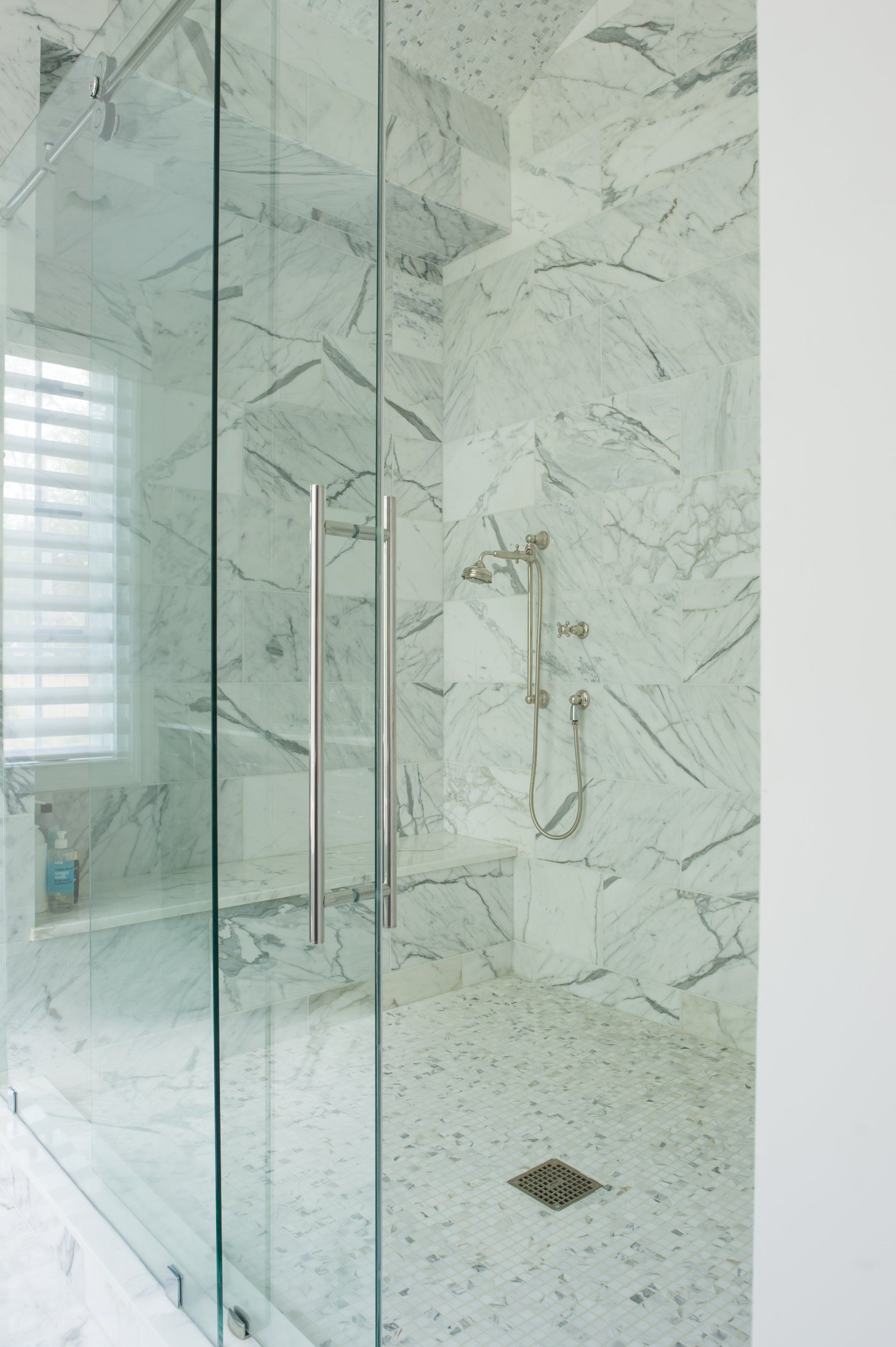 A bathroom with marble tiles and a walk in shower with a glass door.